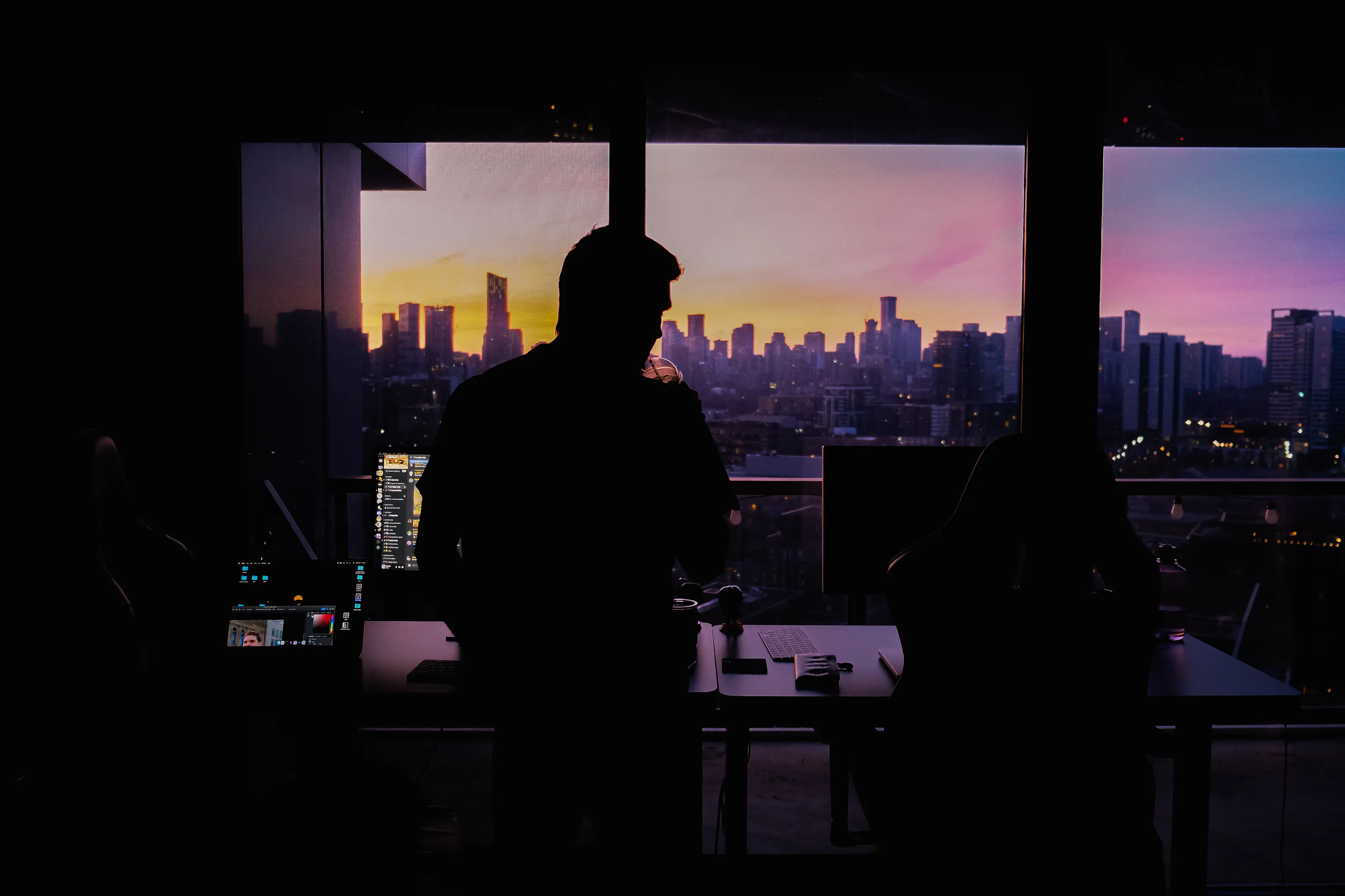 An attorney in silhouette at his desk, the city skyline at dusk behind him