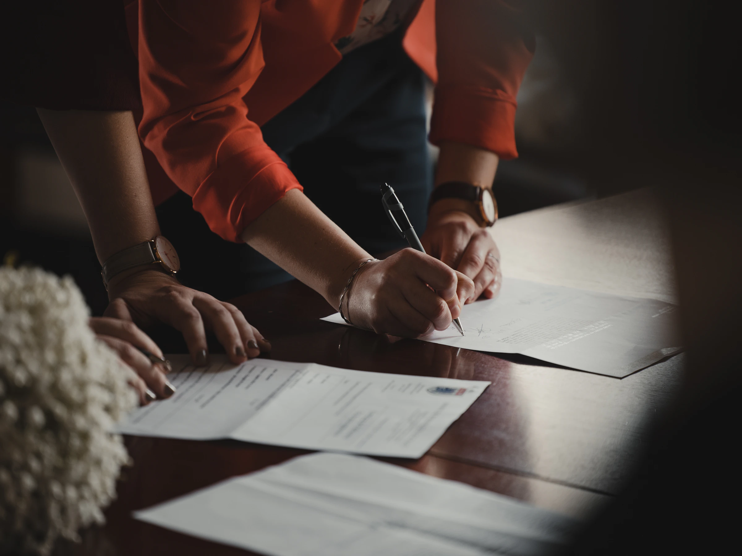 Hands signing an engagement letter at a dark wooden table